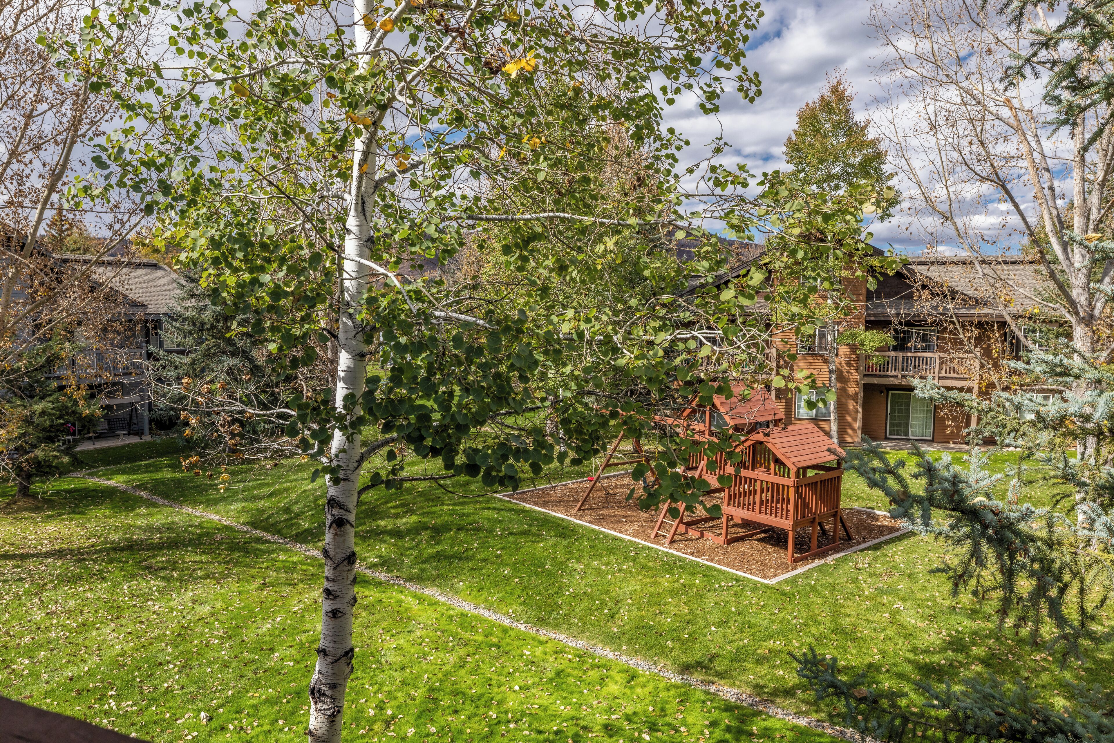 A backyard with a wooden playset, a well-maintained lawn, and a house with a brick exterior.