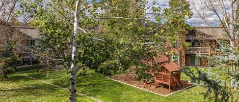 A backyard with a wooden playset, a well-maintained lawn, and a house with a brick exterior.