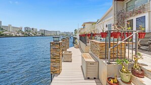 A waterfront balcony with potted plants, a stone pathway, and a view of the city skyline.