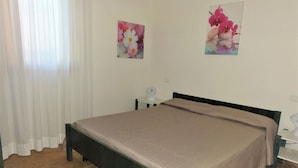A bedroom with a bed, a nightstand, a lamp, and two floral wall art pieces. - Comfy Villa With Fenced Garden Near the Beach (San Michele al Tagliamento)