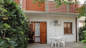 A two-story building with a wooden balcony, a white door, and a small outdoor seating area with plastic chairs. - Flat in a Villa With Private Garden (San Michele al Tagliamento)