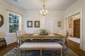 A dining room with a wooden table, cushioned bench, and a chandelier.