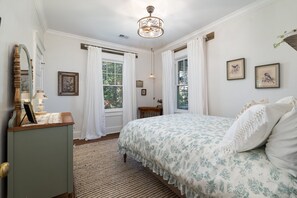 A bedroom with a bed, a dresser, a mirror, and two windows with curtains.