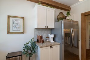 A kitchen with white cabinets, a stainless steel refrigerator, a coffee maker, and a framed botanical illustration on the wall.