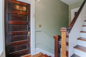Una puerta de madera con el número '3' en la pared contigua, una escalera con barandillas de madera y una pared de color verde claro.