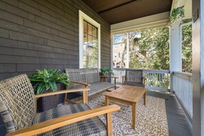 Un porche cubierto con muebles de mimbre, una mesa de madera y plantas en macetas.