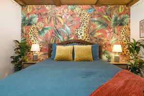 Een bed met een blauw laken, twee gele kussens en een houten hoofdbord. Er staan twee nachtkastjes met lampen en potplanten.