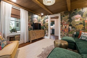 Una sala de estar acogedora con techo de madera, un sofá verde, un tapete estampado y un televisor sobre un mueble de madera.