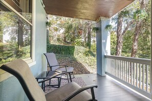 Un espace extérieur abrité, aménagé avec deux chaises et une table, donnant sur un jardin agrémenté d’arbres et d’une haie.