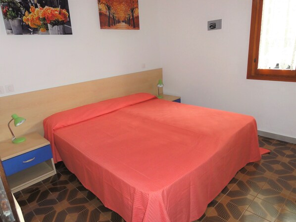 Une chambre à coucher avec un lit, une table de chevet, une lampe et un mur orné d’un tableau.