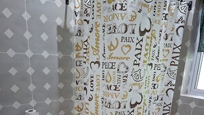 Ein Badezimmer mit Duschvorhang, der die Wörter 'love' und 'peace' zeigt, einer Toilette und einem grünen Handtuch.