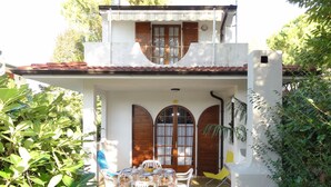 Ein zweistöckiges Haus mit einer Terrassenfläche, die ein Tisch und Stühle umfasst, umgeben von viel Grün.