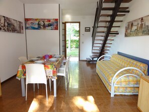 Un comedor con una mesa lista para cuatro personas, un sofá y una escalera que lleva a un área exterior.