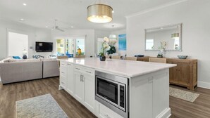 Une cuisine moderne avec des meubles blancs, un îlot central, un four à micro-ondes encastré et un luminaire suspendu.