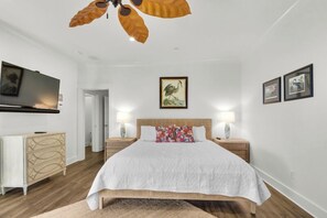 Un dormitorio con cama, mesitas de noche, televisor y obras de arte en las paredes.
