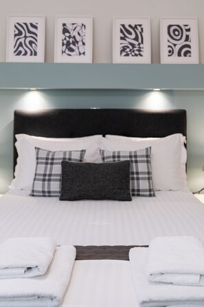 A neatly made bed with white linens, a black headboard, and a grey pillow.