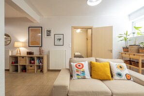 A cozy living room with a sofa, cushions, a bookshelf, a lamp, and a door leading to another room. - Stylish 2Bedroom Apt at the foothills of Acropolis (Athina)