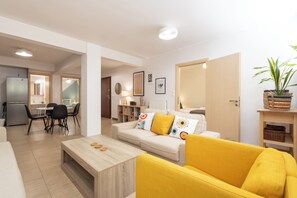 A modern living room with a yellow sofa, a wooden coffee table, and a dining area with a table and chairs.