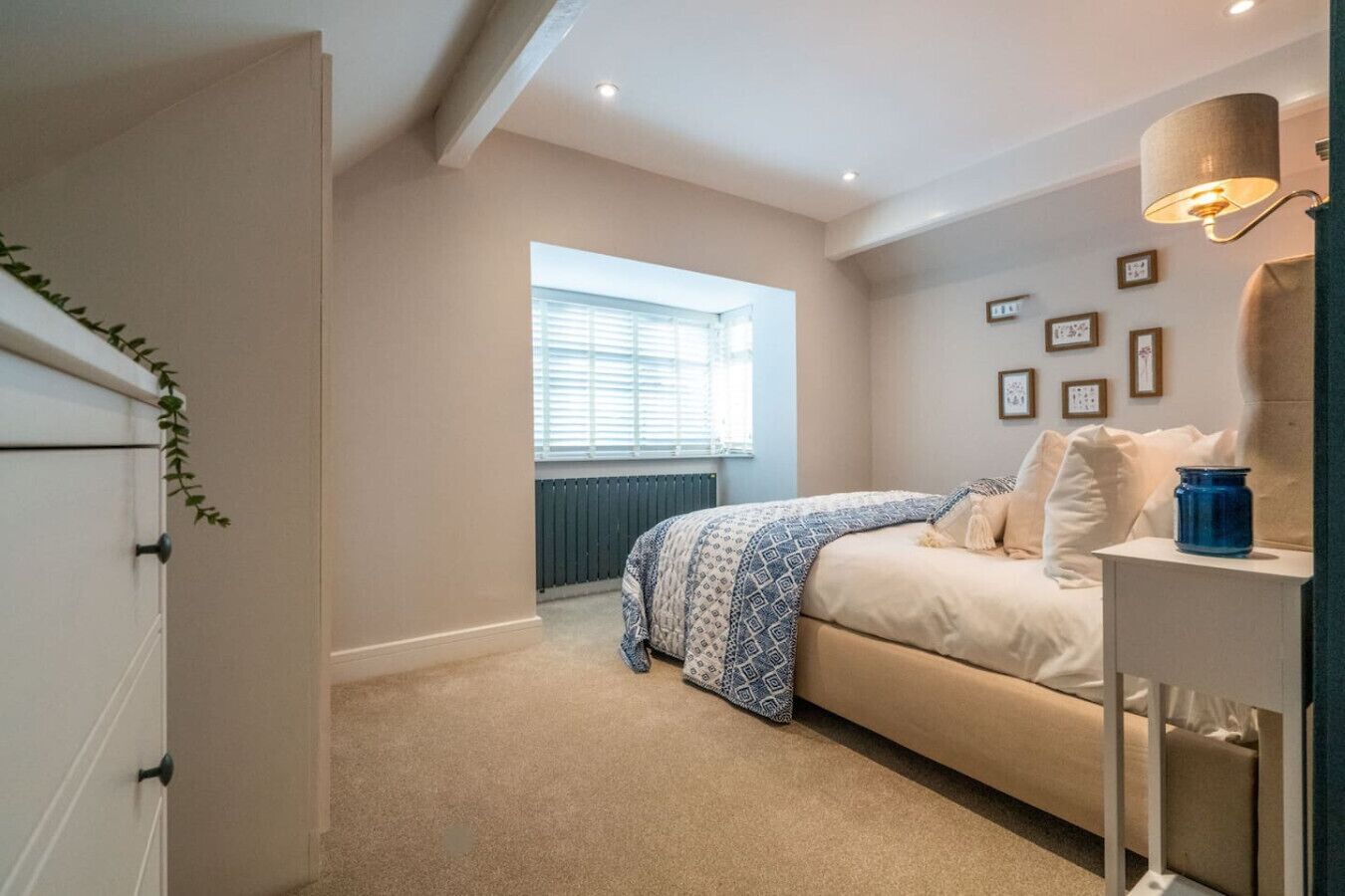 A bedroom with a bed, a bedside table, a lamp, and a window with blinds.