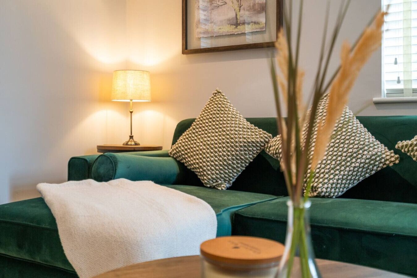Un divano verde con cuscini strutturati, una coperta bianca e un tavolino con un vaso e una candela.
