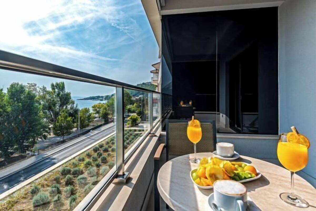 Un balcon avec une table préparée pour le petit-déjeuner, une vue sur la côte et un ciel dégagé.