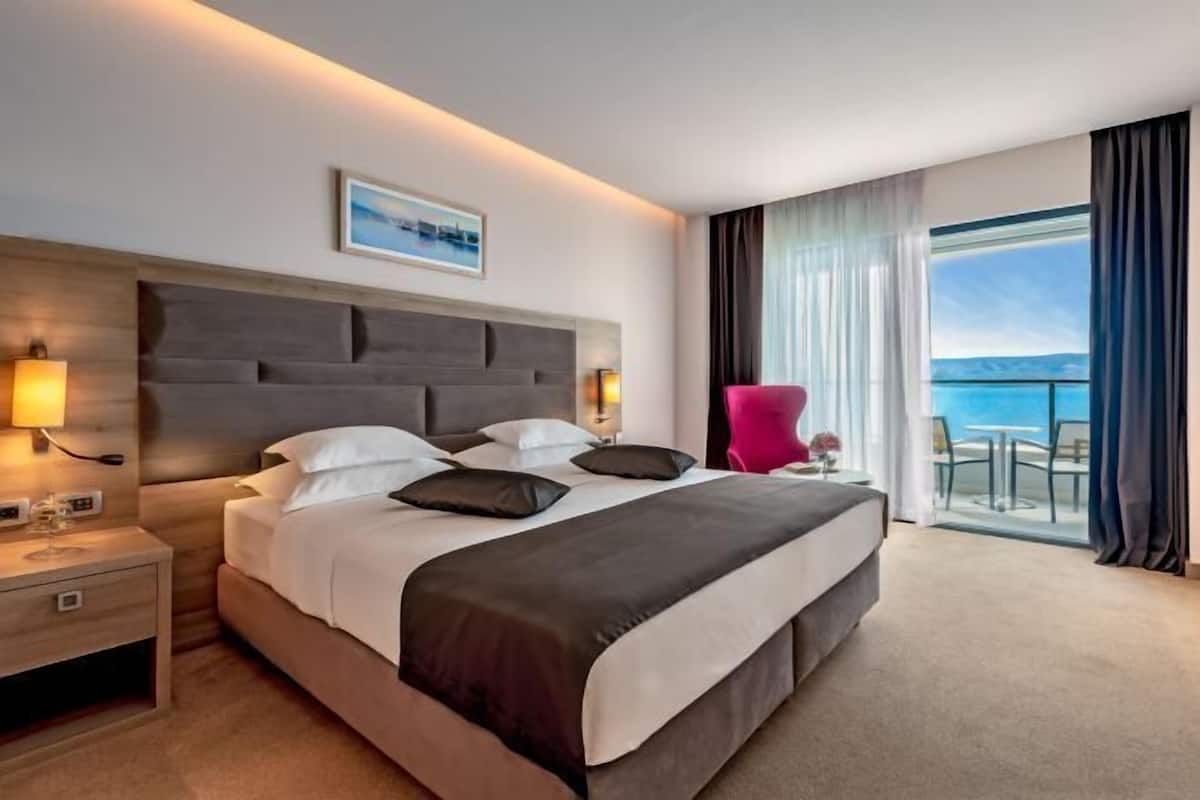 Une chambre d’hôtel avec un grand lit, une table de chevet, une chaise et un balcon avec vue.