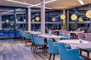 Un restaurant avec des tables et des chaises, de grandes fenêtres et des luminaires suspendus.
