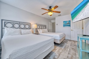 Ein Hotelzimmer mit zwei Betten, einem Deckenventilator, einem Gemälde und Blick auf einen Strand.