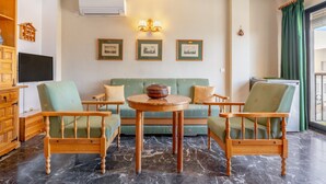 Una sala de estar con un sofá verde, sillas de madera, una mesa redonda de madera y cuadros enmarcados en la pared.