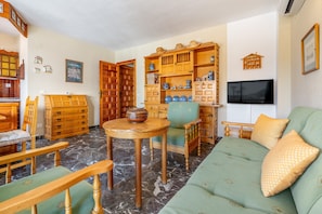 A living room with a green sofa, wooden furniture, a TV, and a bookshelf.