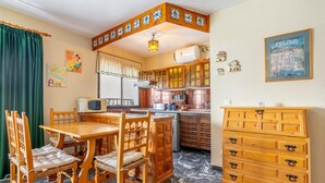 Una cocina con armarios de madera, una mesa de comedor con sillas, un microondas y un refrigerador.