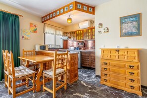 Una cocina con armarios de madera, una mesa de comedor con sillas, un microondas y un refrigerador.