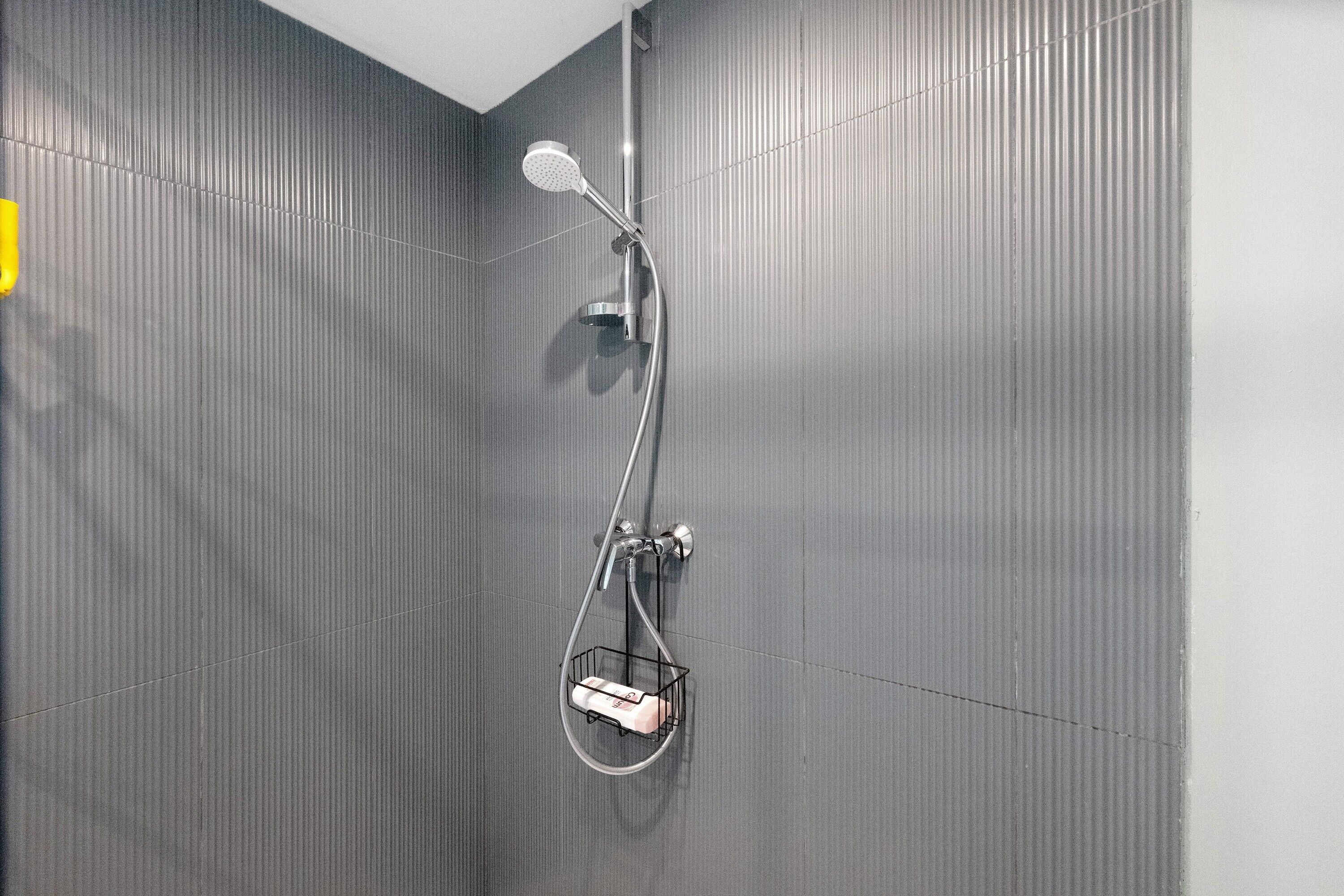 Doccia con soffione manuale e irrigatore a mano, montati su una parete con rilievi verticali.