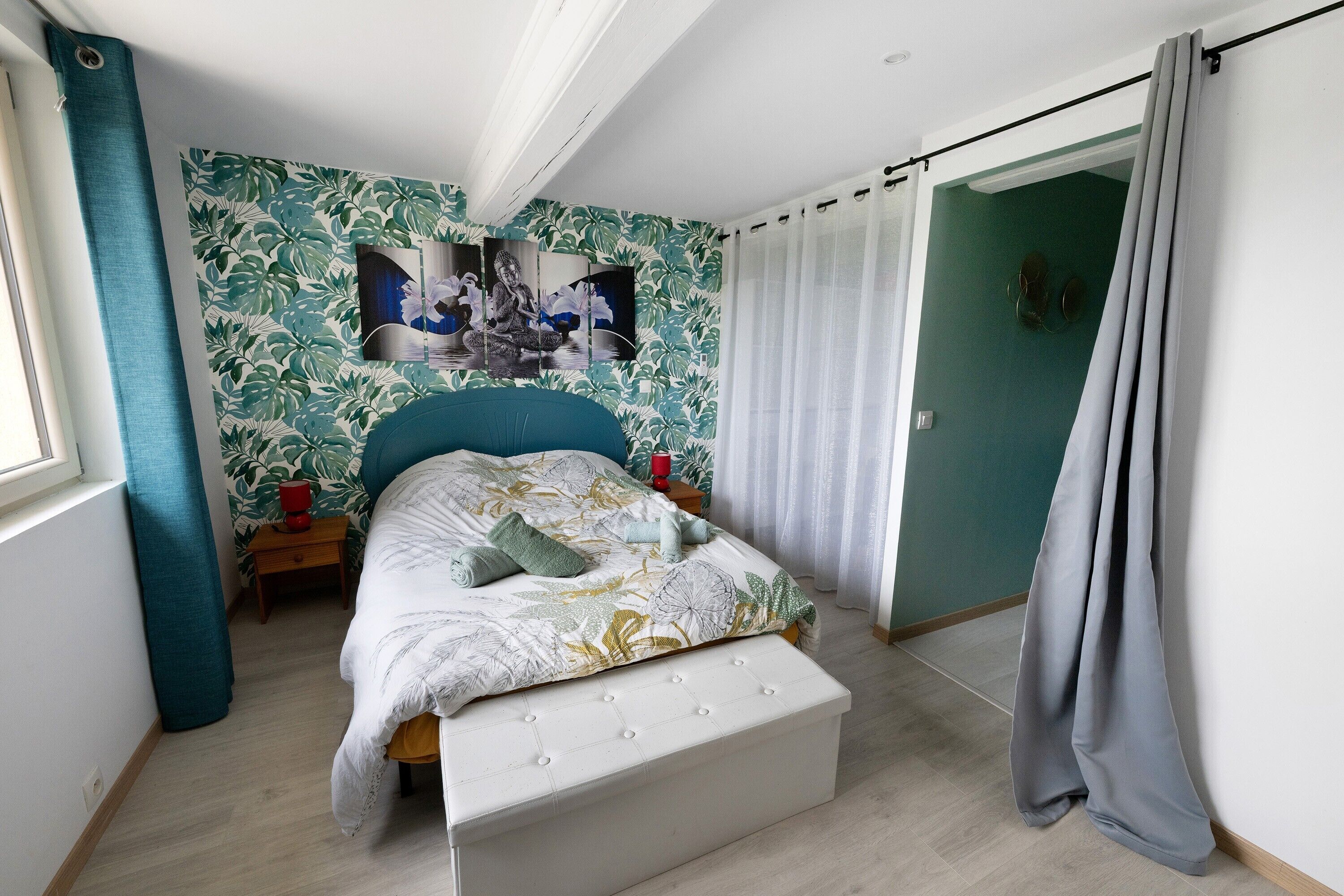 Um quarto com cama, mesa de cabeceira, parede com padrão floral e porta com cortinas.