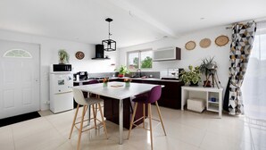 A modern kitchen with a dining area, white cabinetry, and a large window. - Gîte 'Gite Villarnoux' with Private Terrace, Wi-Fi and Air Conditioning (Bussières)