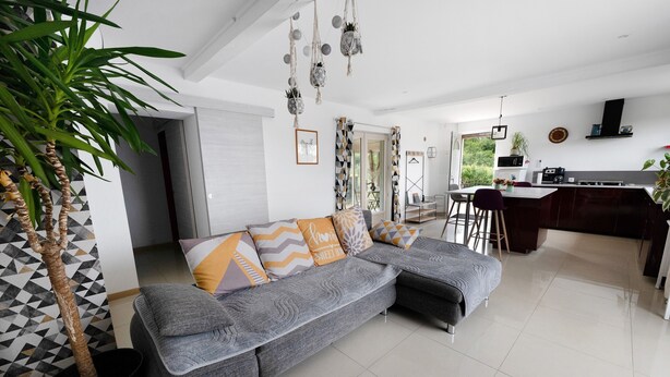 A modern living room with a grey sectional sofa, a potted plant, and a kitchen area with a dining table and chairs. - Gîte 'Gite Villarnoux' with Private Terrace, Wi-Fi and Air Conditioning (Bussières)