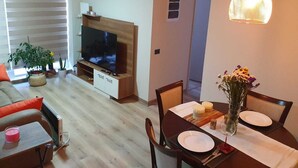 A living room with a TV, wooden entertainment unit, and a dining area with a table set for two. - Fully equipped apartment, bedroom en suite in Valdivia, direct access to the city entrance. (Valdivia)