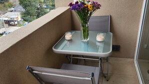 A small balcony with a glass table and metal chair, a vase with flowers, and candles. - Fully equipped apartment, bedroom en suite in Valdivia, direct access to the city entrance. (Valdivia)