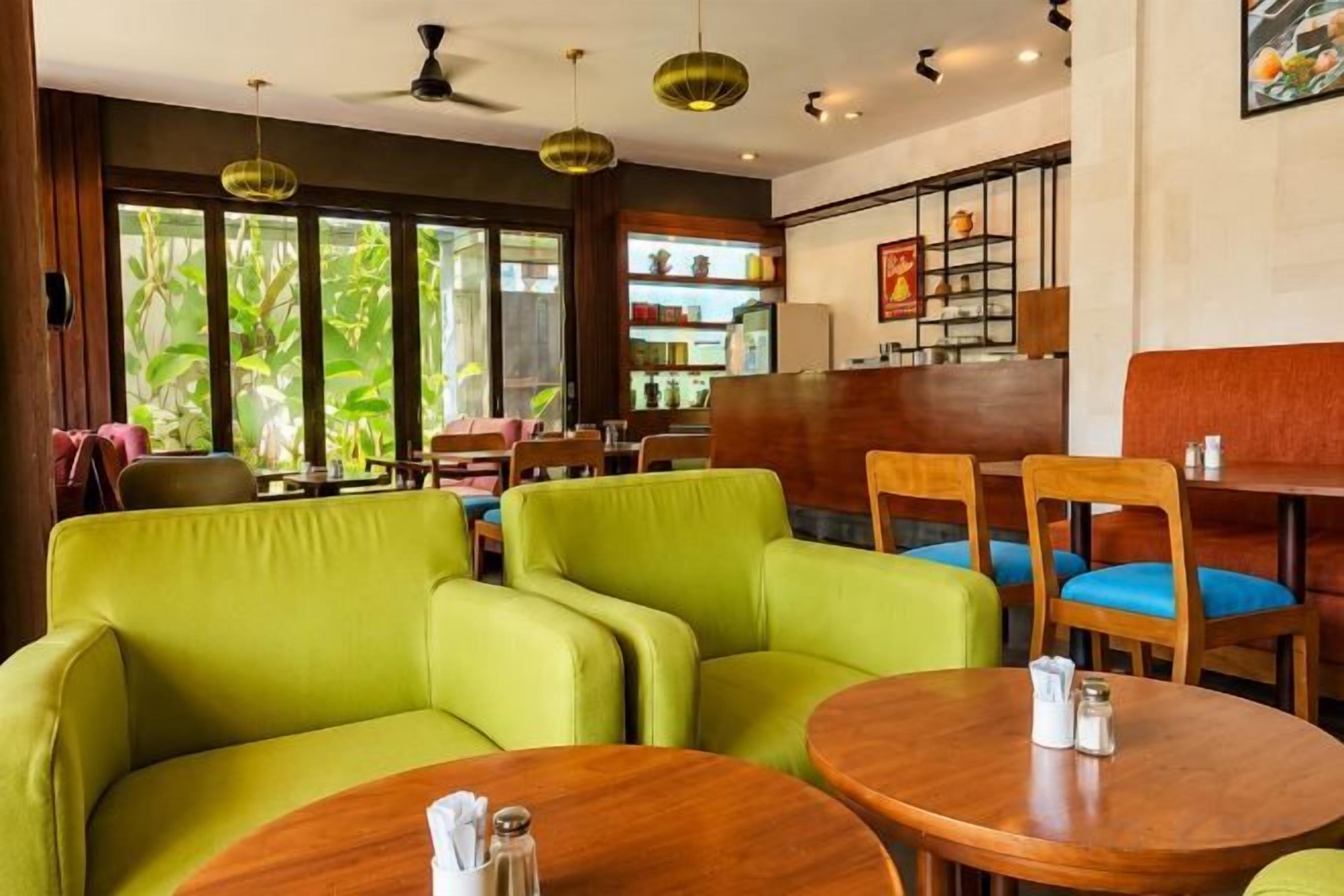 Een restaurant met groen gestoffeerde zitplaatsen, houten tafels en uitzicht op groen.