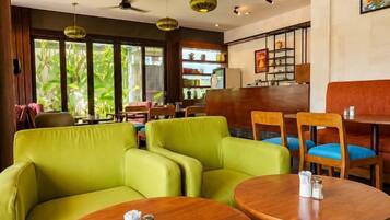 Een restaurant met groen gestoffeerde zitplaatsen, houten tafels en uitzicht op groen.
