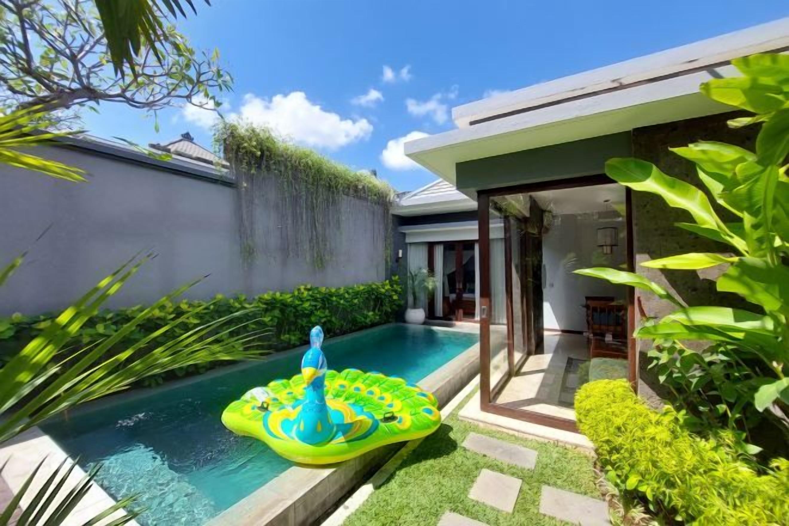 A swimming pool with a water feature and a floating platform, surrounded by greenery and a modern house.