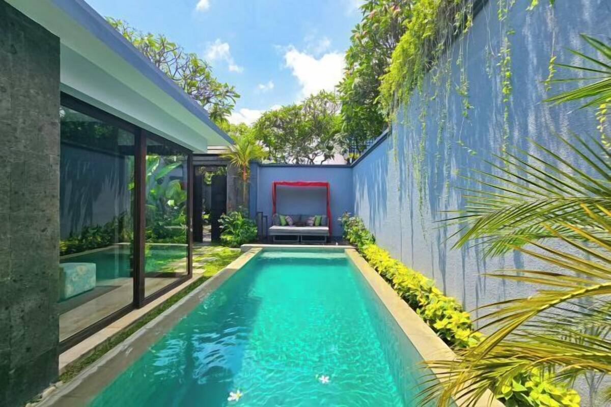 A modern pool area with a glass wall, a red-framed seating area, and lush greenery.