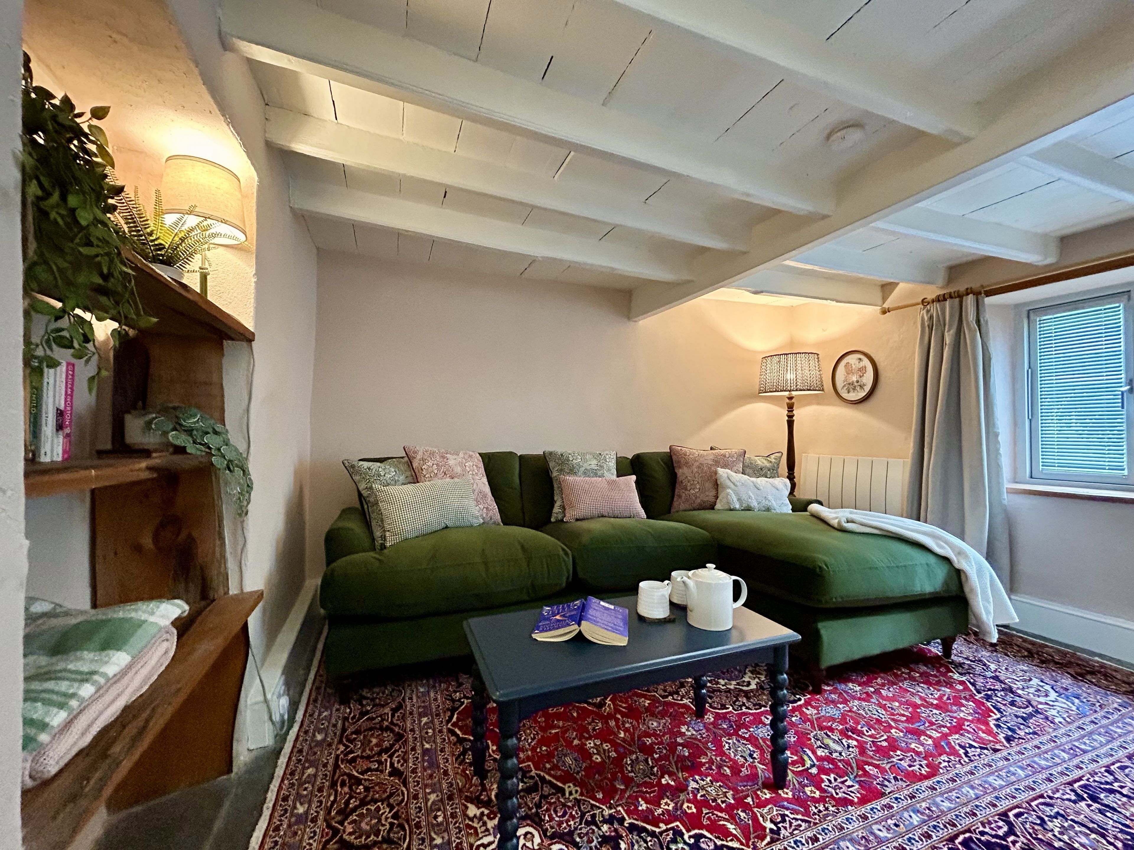 Een gezellige woonkamer met een groene bank, een klein tafeltje, een vloerkleed met dessin en een boekenkast.