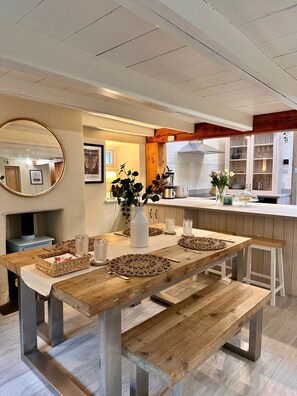 A modern kitchen with a wooden dining table, benches, and a central island. - Pilgrim Cottage - sleeps 4 guests  in 2 bedrooms (Newquay)