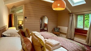 A bedroom with a skylight, a large bed with multiple pillows, a bedside table, and a chair. - Pilgrim Cottage - sleeps 4 guests  in 2 bedrooms (Newquay)