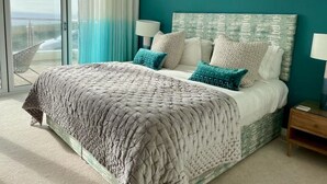 A bedroom with a large bed, a view through the glass door, and a teal accent wall.