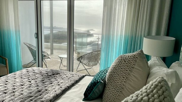A bedroom with a bed, pillows, a lamp, and a view of the outdoors through a sliding door.