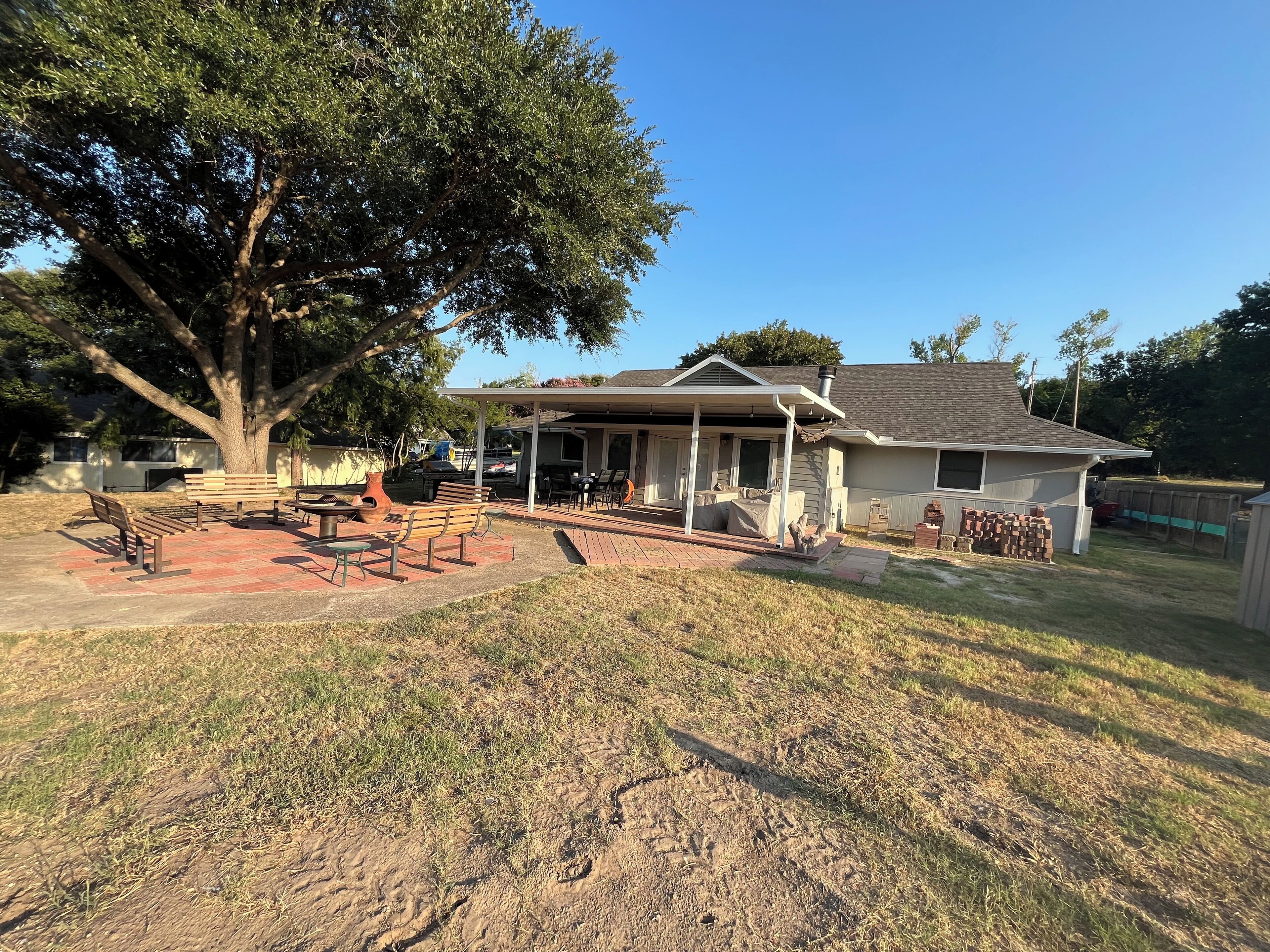 A house with a covered patio, a large tree, and a brick patio area.