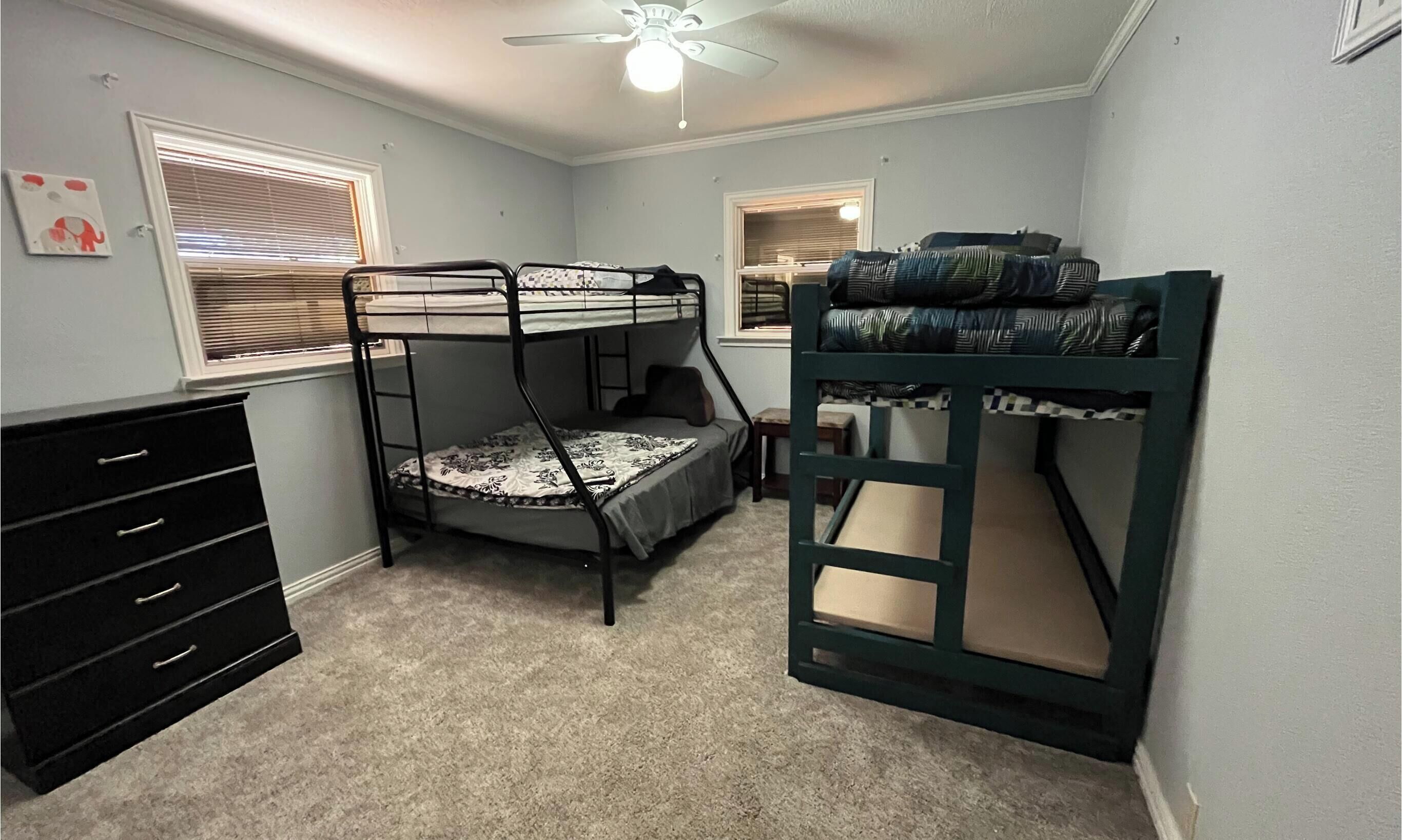 A room with bunk beds, a dresser, a window with blinds, and a ceiling fan.