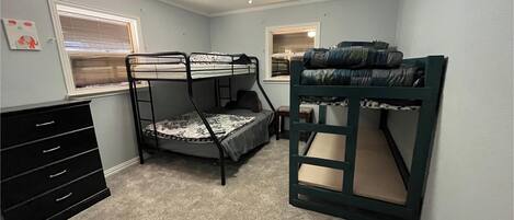 A room with bunk beds, a dresser, a window with blinds, and a ceiling fan.